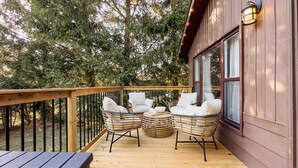 A wooden deck with wicker furniture and a table, overlooking a forested area. - Cameron's Peaceful Pines, King Bed! (Bayfield)