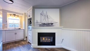 A kitchen with white cabinetry, a fireplace, and a large painting of a sailboat. - Cameron's Peaceful Pines, King Bed! (Bayfield)