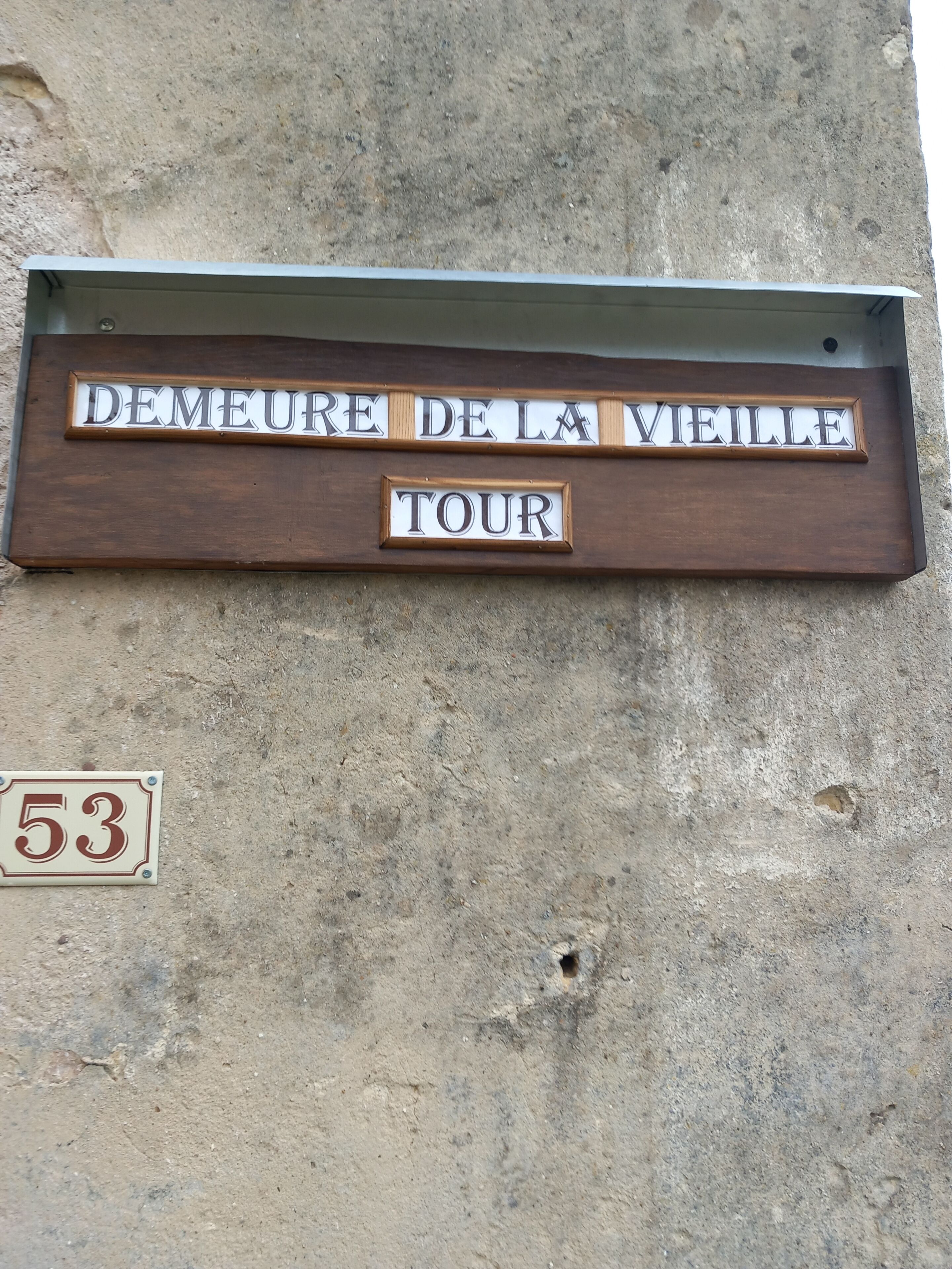 A wooden sign with the text "DEMEURE DE LA VIEILLE TOUR" mounted on a concrete wall.
