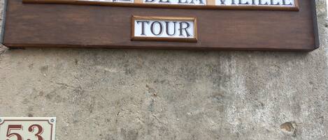 A wooden sign with the text "DEMEURE DE LA VIEILLE TOUR" mounted on a concrete wall.