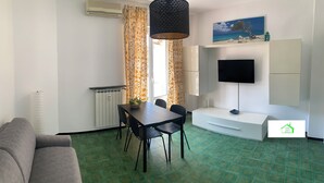 A room with a sofa, a dining table with chairs, a TV mounted on the wall, and a radiator. - Lavi House with Box (Rapallo)