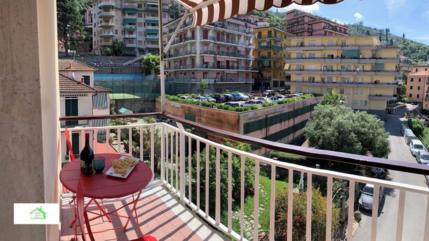 A balcony with a red table and chairs, overlooking a parking area and multi-story buildings. - Lavi House with Box (Rapallo)