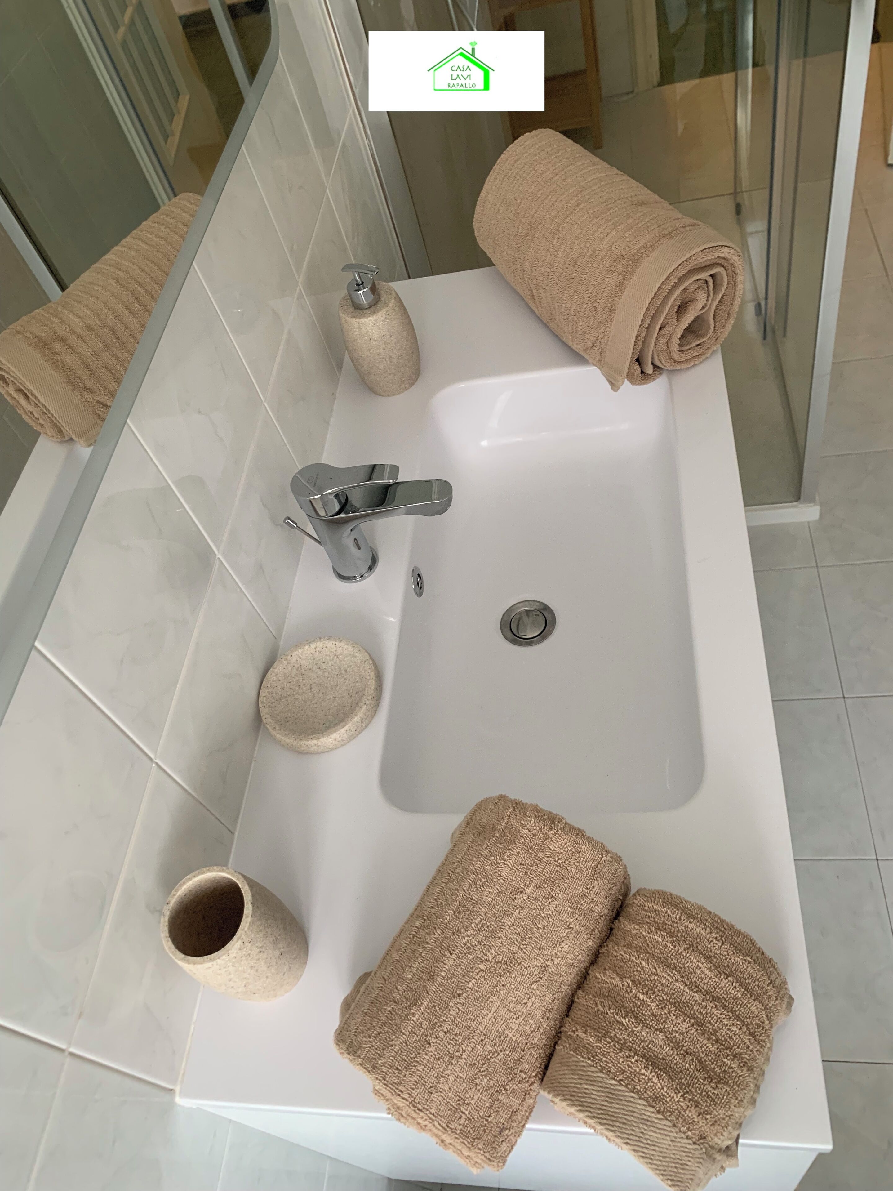 Une salle de bain avec un lavabo blanc, une serviette, un distributeur de savon et un gobelet.