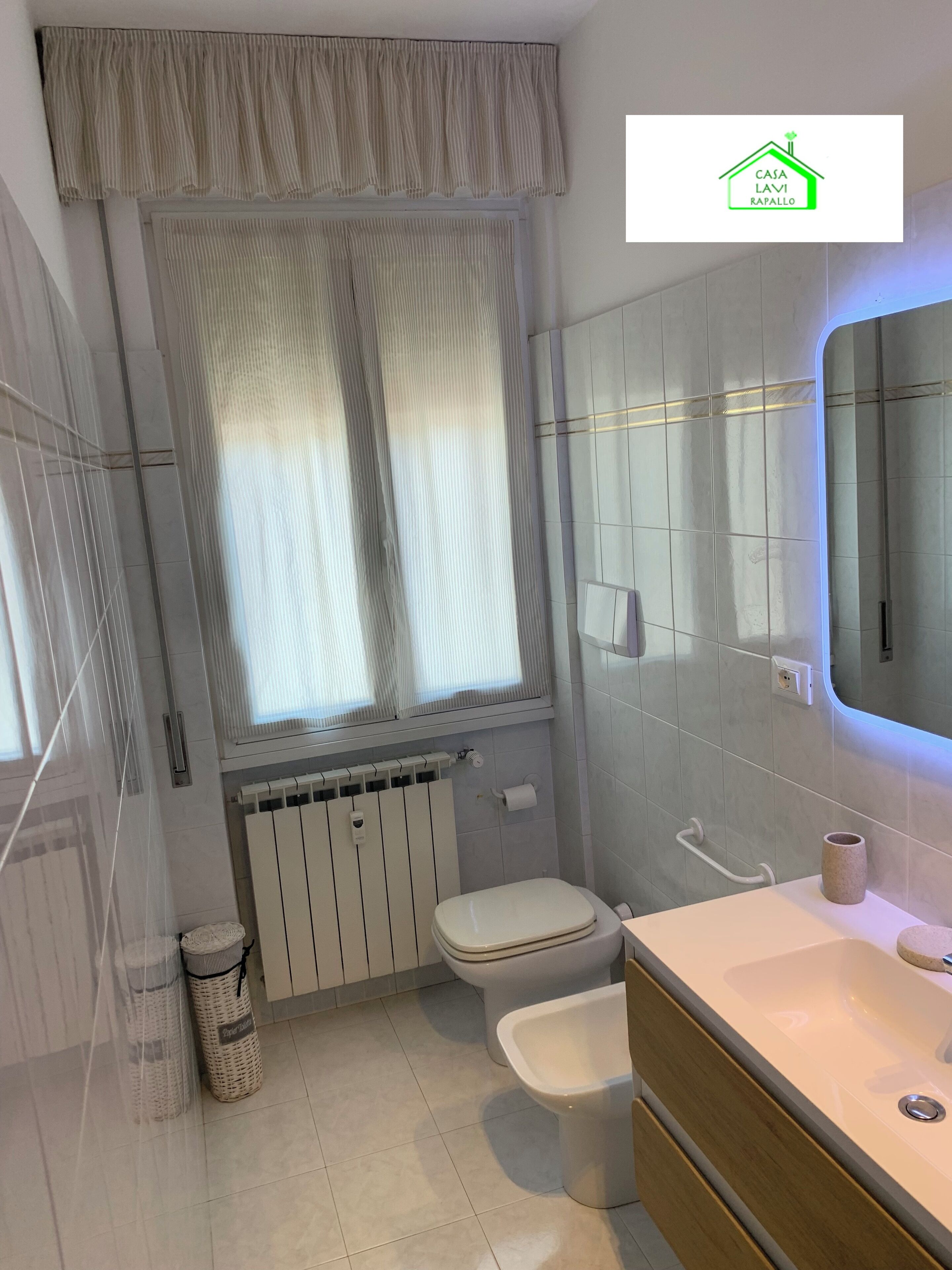 Un baño moderno con inodoro, bidé, tocador y una ventana con cortinas.
