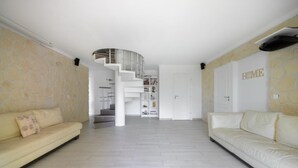 Ein geräumiger Wohnbereich mit Treppe zu einer oberen Ebene, einem weißen Sofa und einem Bücherregal.