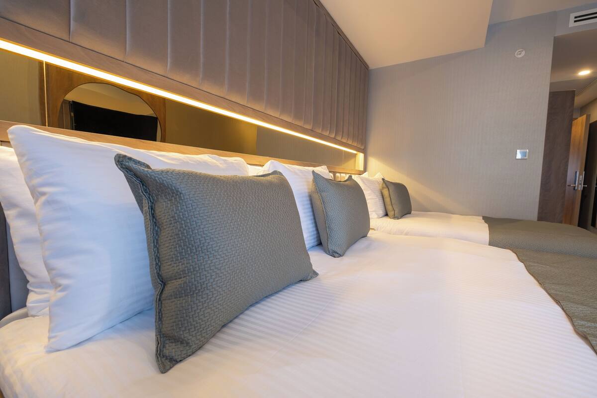A hotel room with a large bed, a headboard with built-in lighting, and a mirror above the bed.