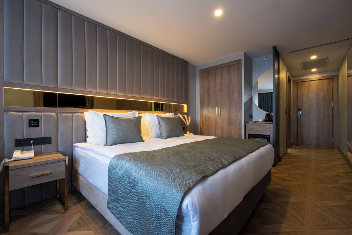 A modern hotel room with a large bed, a bedside table, a wardrobe, and a mirror.