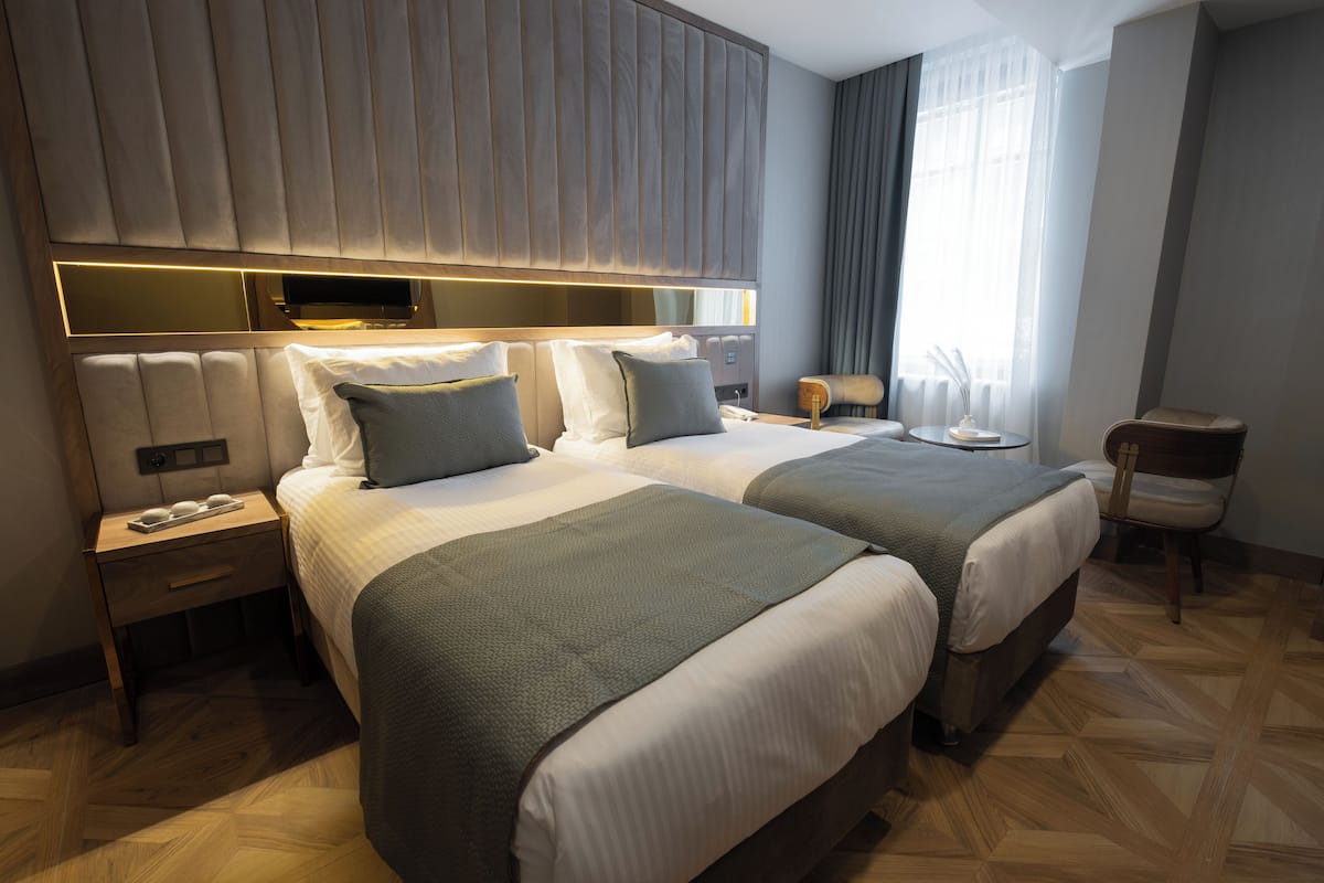 A modern hotel room with two beds, a wooden headboard, a bedside table, a nightstand, and a chair.