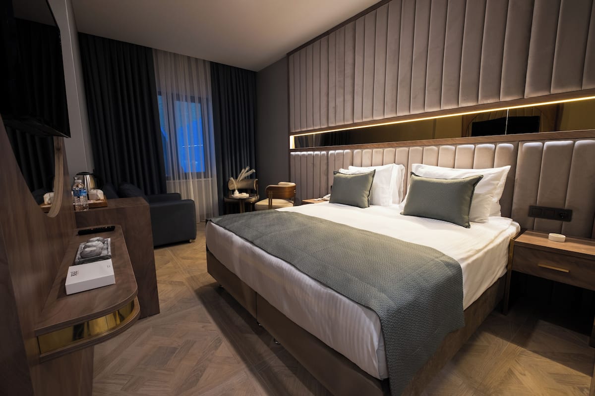 A modern hotel room with a large bed, a bedside table, a nightstand, a desk, and a chair.