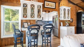 Un acogedor interior de cabaña con paredes de madera, una cocina con armarios blancos y una zona de comedor con sillas azules.