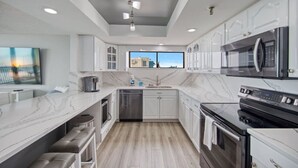 Une cuisine moderne avec des meubles blancs, un plan de travail en marbre, des appareils électroménagers en acier inoxydable et une grande fenêtre offrant une vue sur la ville.