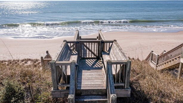 Une promenade en bois mène à une plage où les vagues viennent se briser sur le rivage.