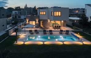 Une maison moderne dotée d’une piscine, d’un espace salon extérieur et d’une terrasse bien éclairée.