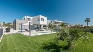 Una moderna casa a due piani con piscina, area salotto esterna e prato curato.