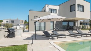 Una moderna casa a due piani con piscina, area salotto esterna e barbecue.