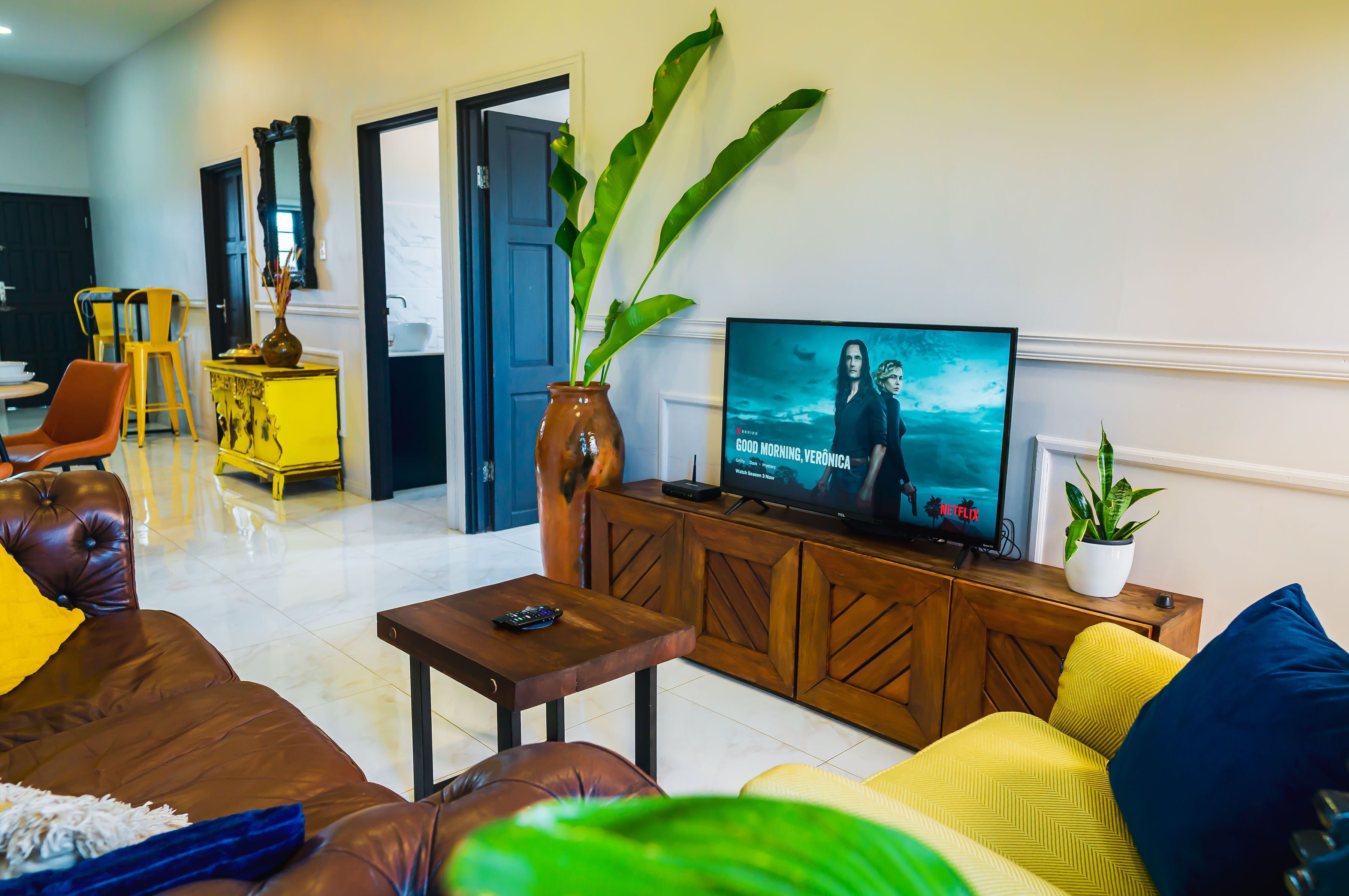 A living room with a TV, sofa, chairs, and a plant.