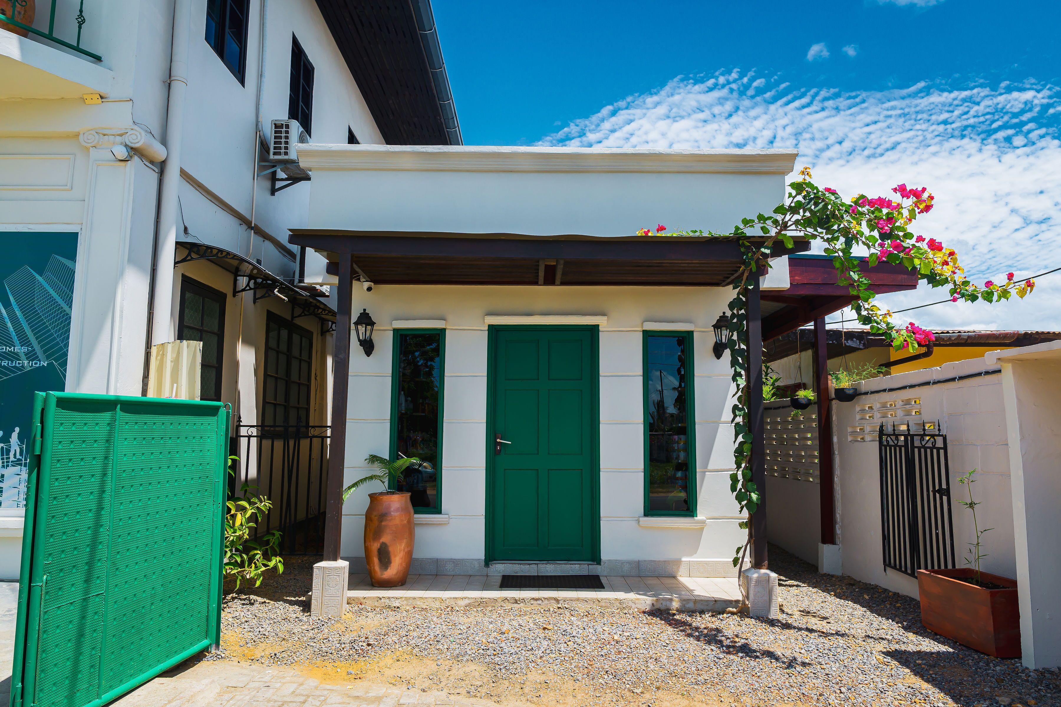 Un edificio blanco con puerta verde, un pequeño porche y un camino de entrada de grava.