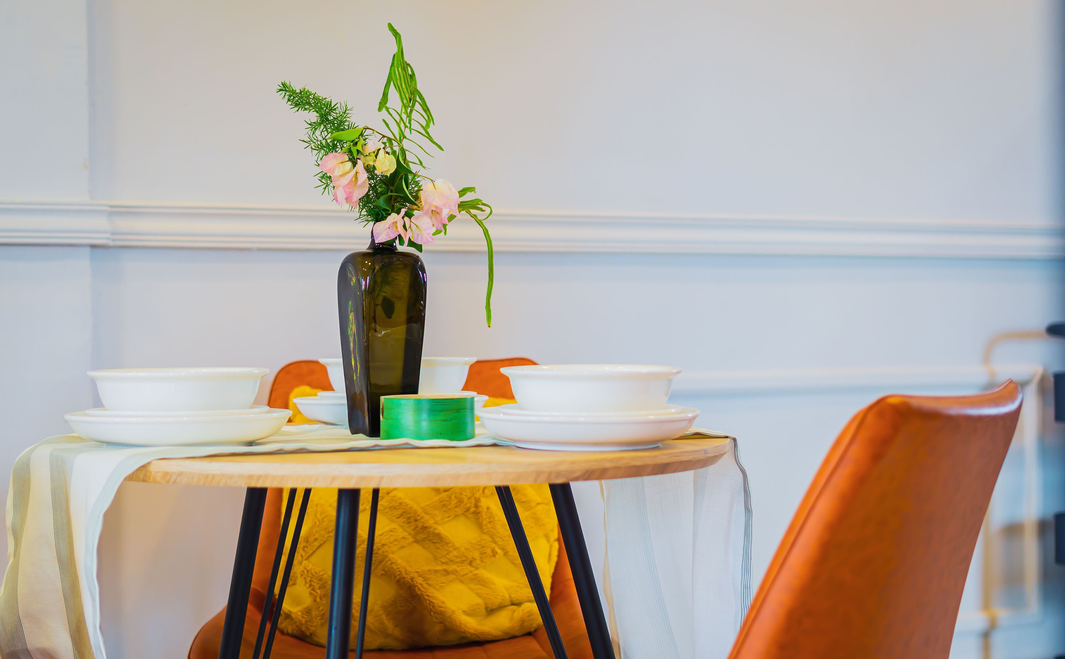 Una mesa de comedor con un florero, platos blancos y un tazón verde.