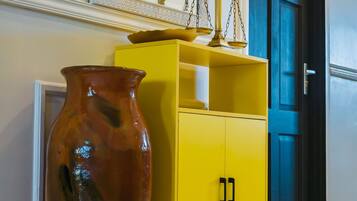 Un mueble amarillo con herrajes negros, un jarrón grande y un espejo encima.