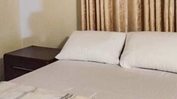 A bedroom with a bed, a nightstand, a headboard, and a window with curtains.