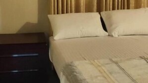 A bedroom with a bed, beige curtains, a wooden nightstand, and a tiled floor. - Blossoms Apartment (Ragama)