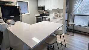 A modern kitchen with white cabinets, a black refrigerator, a microwave, and a large island with stools.