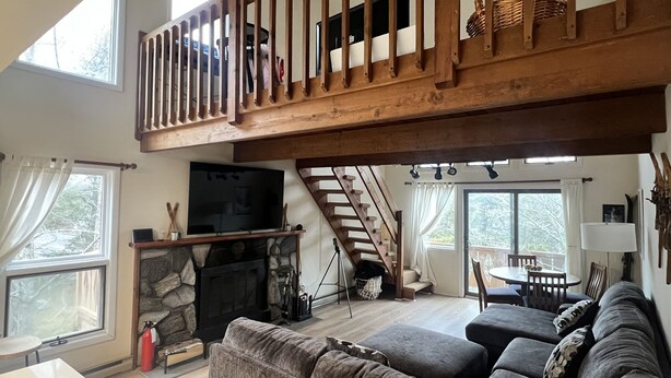 A spacious living area with a stone fireplace, a wooden balcony, and a large TV.