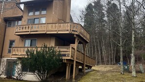 A two-story wooden building with a balcony, surrounded by trees and a grassy area.