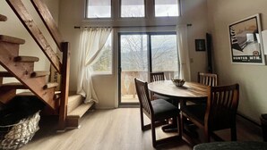 A dining area with a round table and chairs, a staircase with a cat tree, and a large window with curtains.