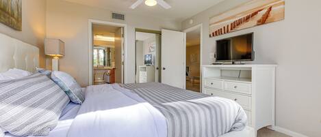 A bedroom with a bed, a ceiling fan, a TV, and a painting on the wall.