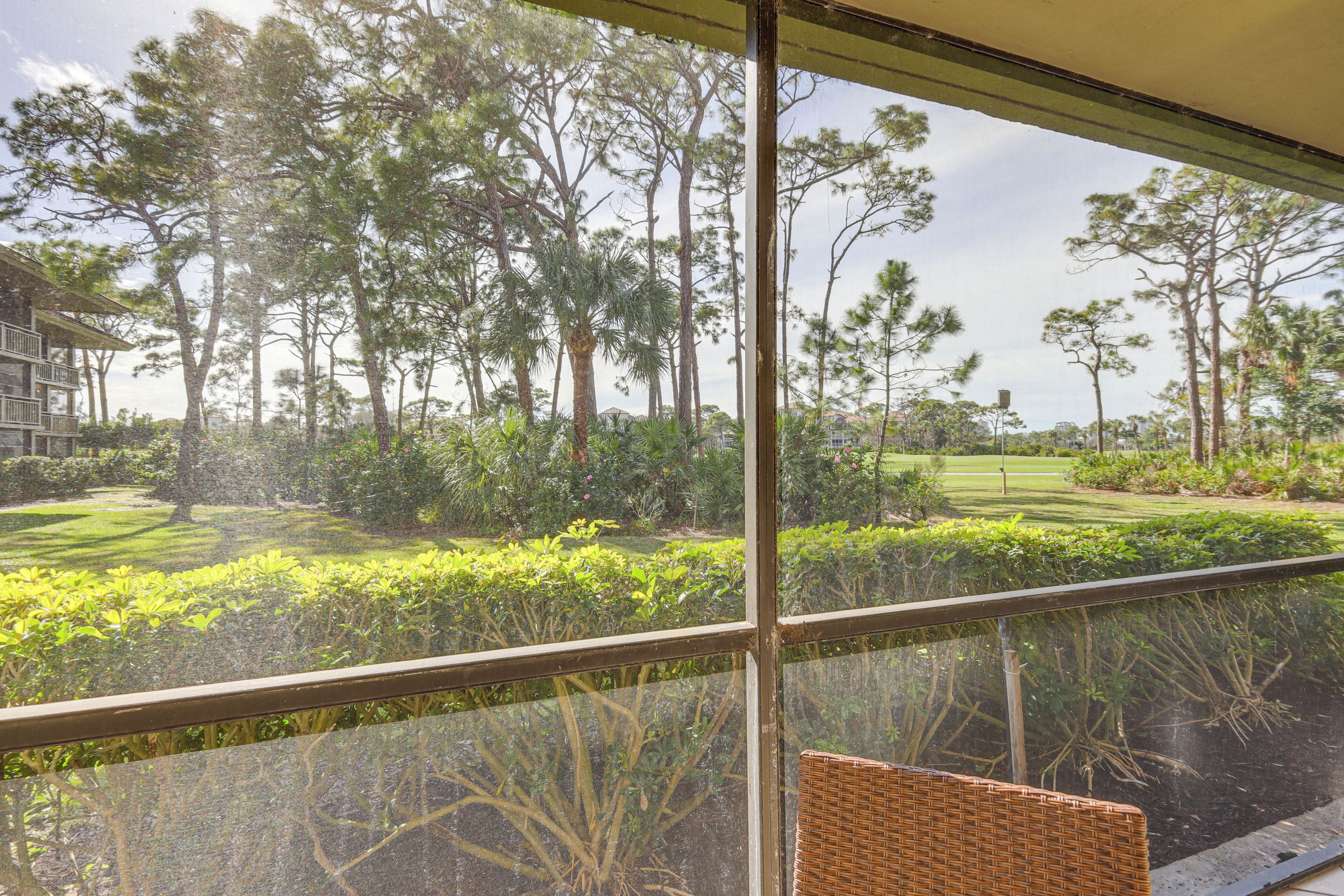 A balcony with a wicker chair, overlooking a well-maintained garden with various trees and shrubs.