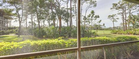 A balcony with a wicker chair, overlooking a well-maintained garden with various trees and shrubs.