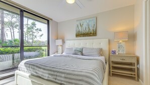 Ein Schlafzimmer mit einem großen Bett, einem Nachttisch mit Lampe, einem Bild an der Wand und Blick ins Grüne durch eine Schiebetür.
