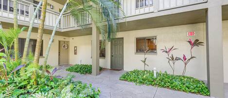 A multi-level building with a central courtyard featuring a stone pathway, surrounded by lush greenery and palm trees.