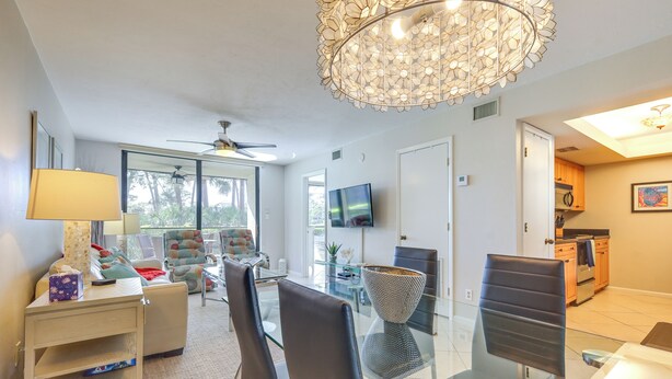 Ein modernes Wohnzimmer mit einem Glastisch, gemütlicher Sitzgelegenheit, einer Chandelierleuchtre und einem an der Wand befestigten Fernseher.