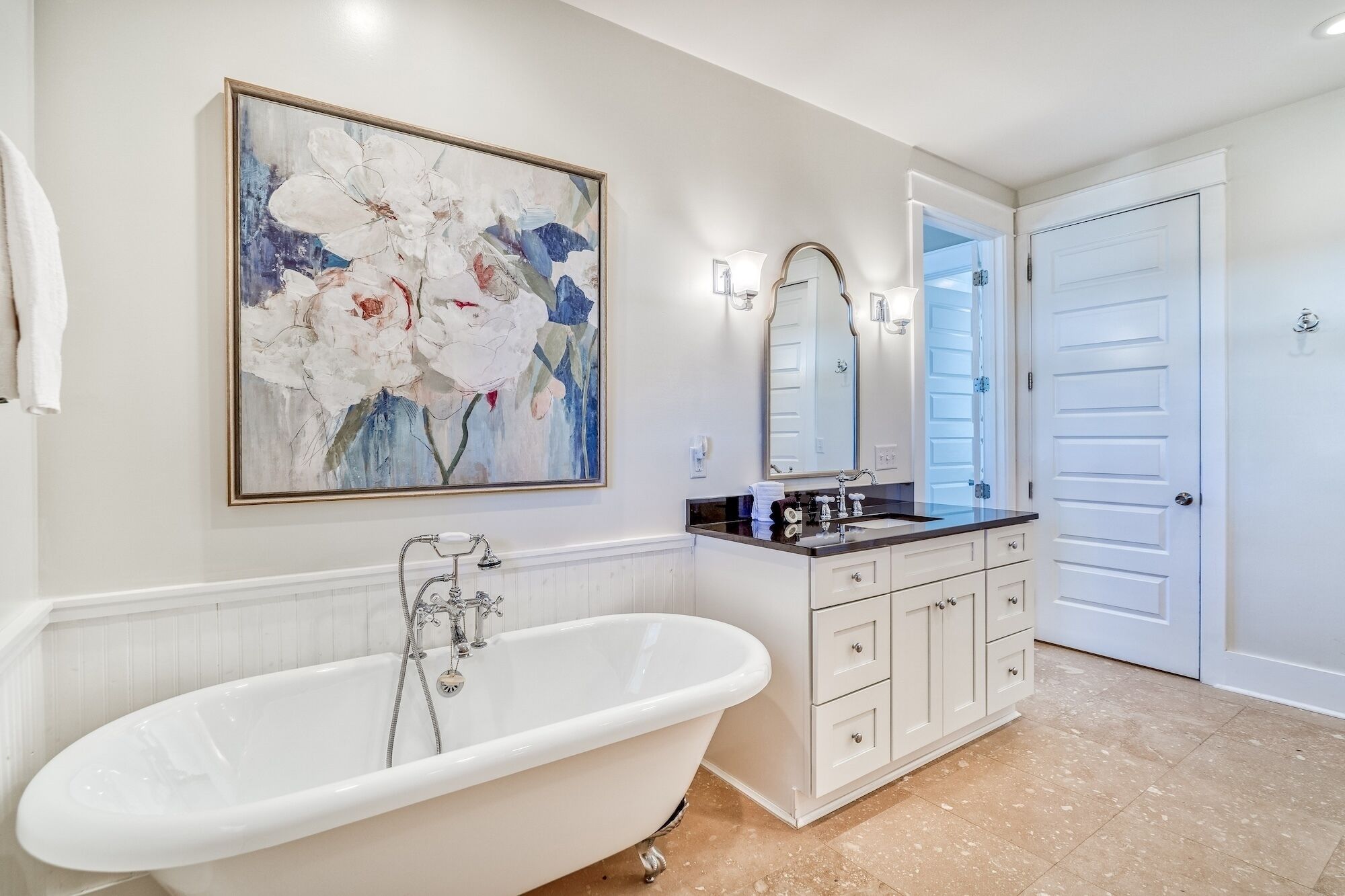A bathroom with a freestanding bathtub, a vanity with a mirror, and a large abstract painting on the wall.