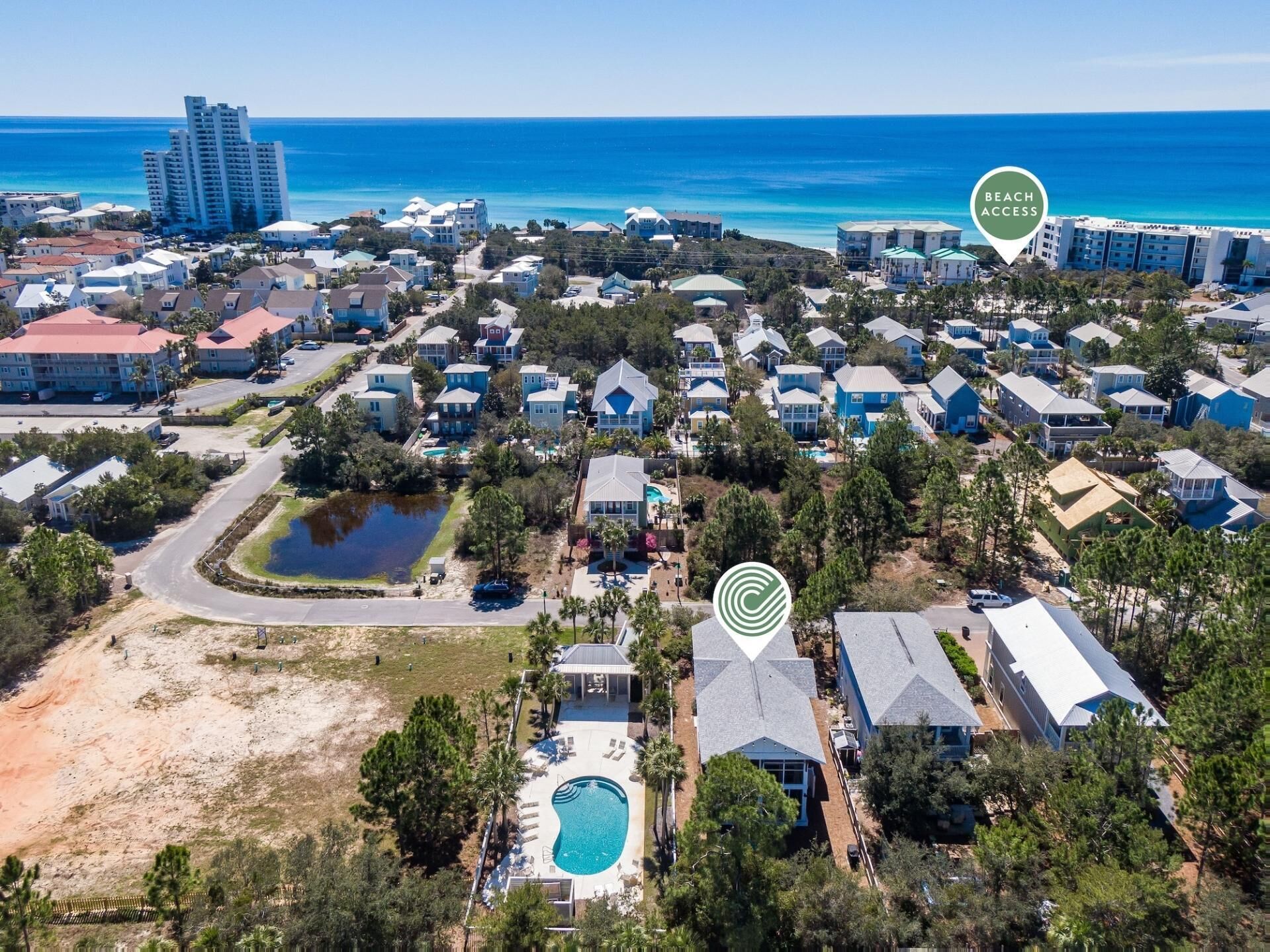 An aerial view of a coastal residential area with houses, a swimming pool, and a beach access sign.