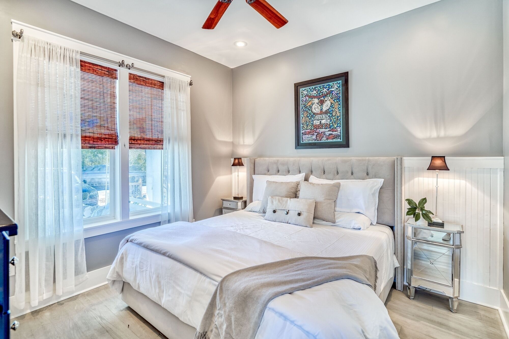 A bedroom with a large bed, two bedside tables, a ceiling fan, and a window with blinds.