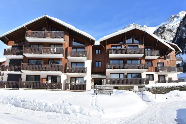 A multi-story wooden chalet with balconies, set against a snowy mountain backdrop.