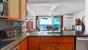 A kitchen with a large island, wooden cabinets, a toaster, and a view of the ocean through large windows. - Big Island Kona Reef D-22 3 Bedroom Condo (Kailua-Kona)