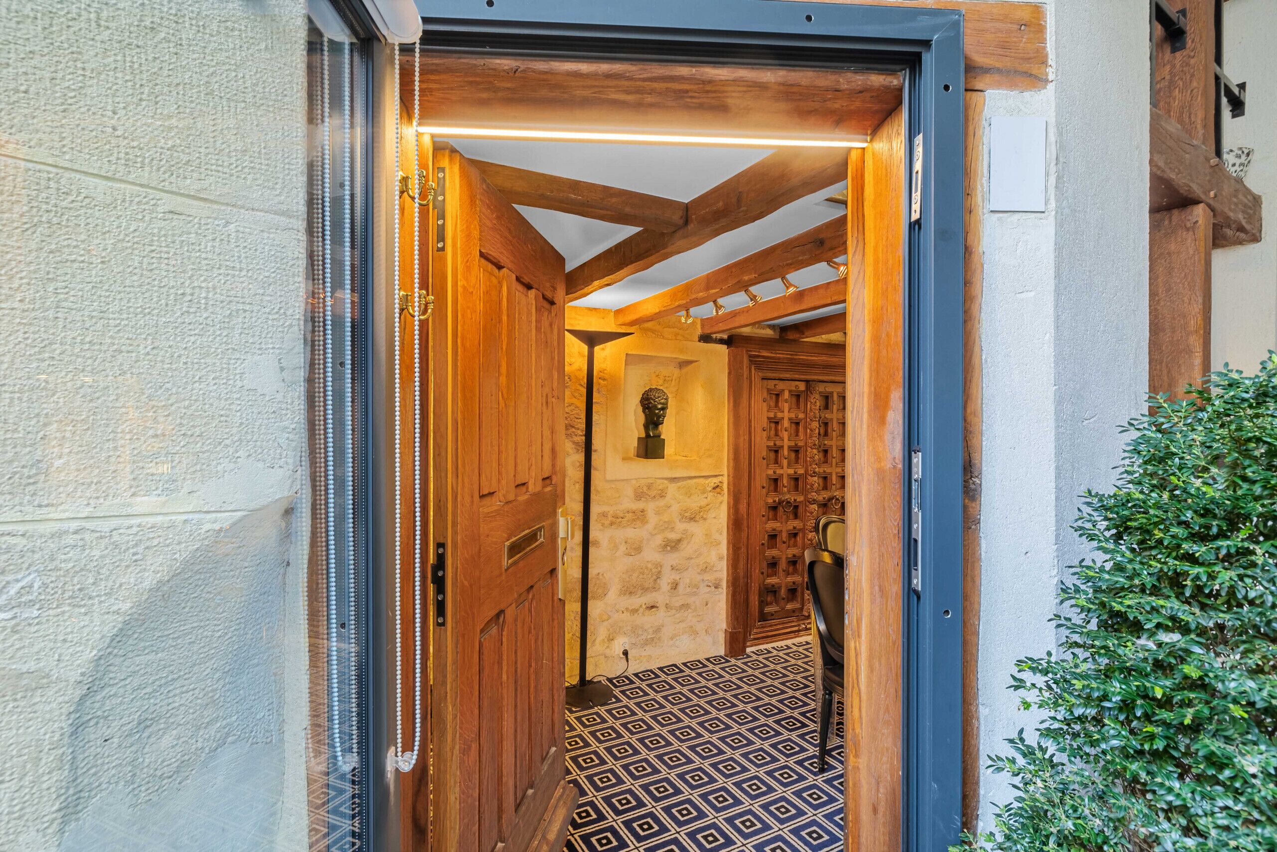 Un couloir avec un sol à motifs, des portes en bois et un mur en pierre.