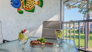 Uma mesa de vidro com duas taças de vinho, um prato de frutas e uma tigela de madeira.