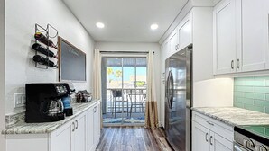 Cozinha com armários brancos, geladeira de aço inoxidável, cafeteira e espaço para vinhos.