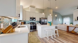 Una cocina moderna con muebles blancos, electrodomésticos de acero inoxidable y una isla central con taburetes.
