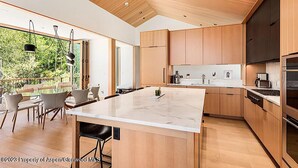 A modern kitchen with wooden cabinets, a large island, and a dining area with chairs.