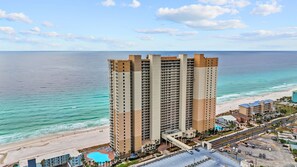A high-rise hotel with multiple floors, a swimming pool, and a beach view.