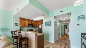 A kitchen with wooden cabinets, a microwave, and a refrigerator. There is a bar area with stools and a counter. The walls are painted teal, and there are decorative signs on the walls.