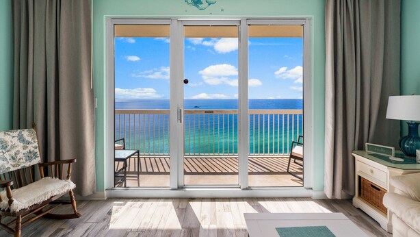 A room with a sliding glass door leading to a balcony with a view of the ocean.