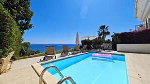 Ein Pool mit Liegestühlen und Sonnenschirmen mit Blick auf das klare, blaue Meer.