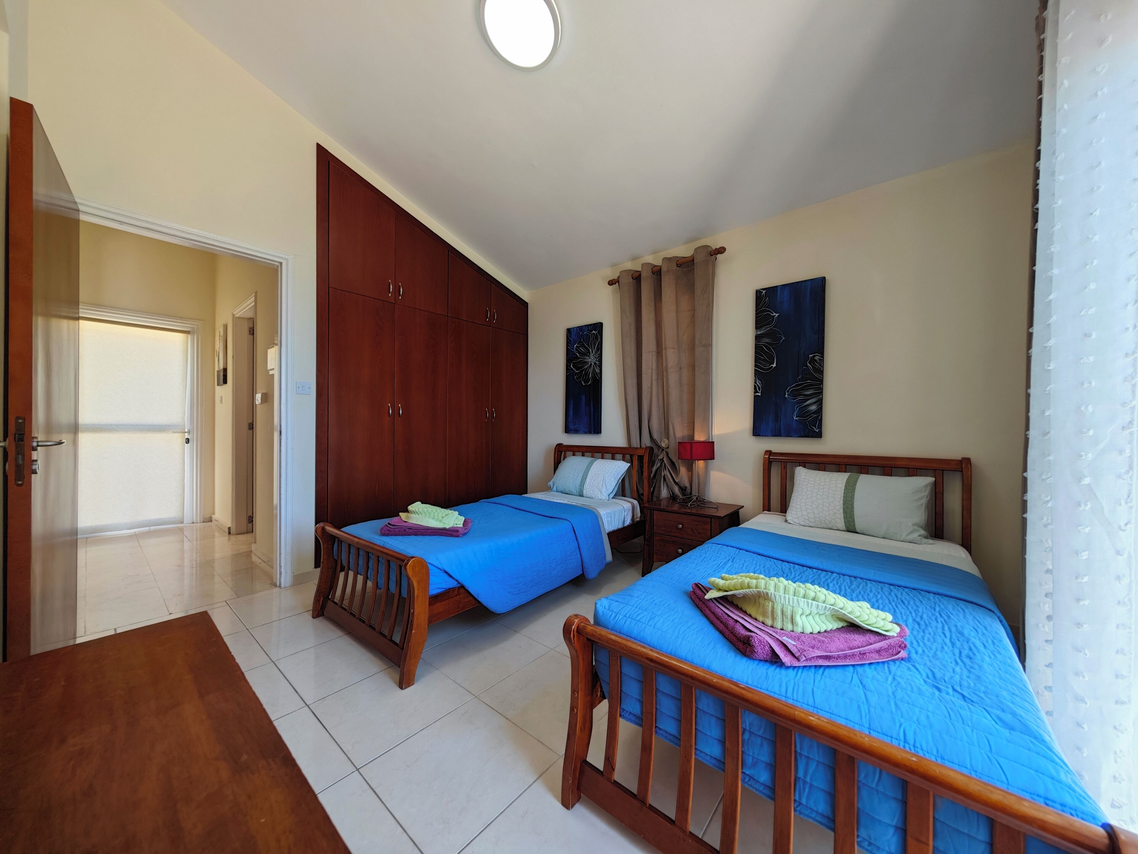 A bedroom with two beds, a wardrobe, and a door leading to another room.